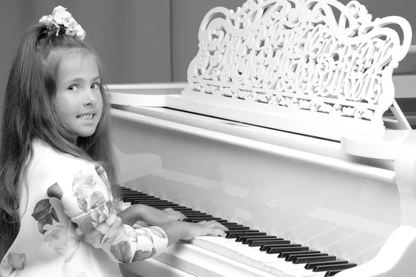 Beautiful little girl is playing on a white grand piano.