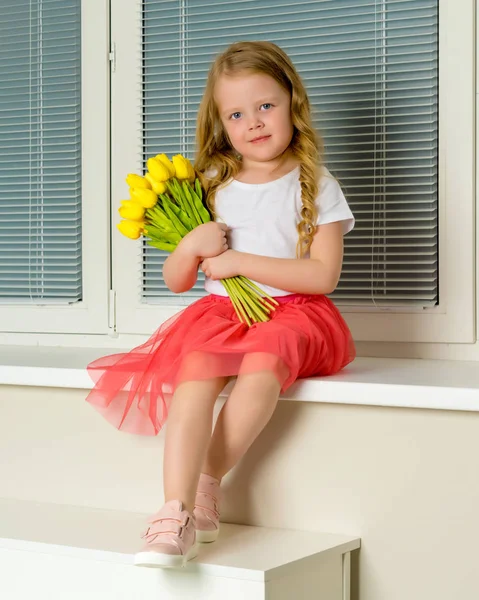 A little girl is sitting on the windowsill with a bouquet of tul — Stock Photo, Image