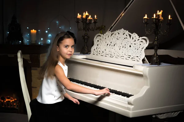 A teenage girl plays a piano on a Christmas night by candlelight