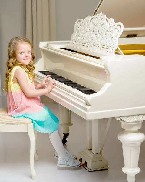 A menina está no piano de cauda branco. — Fotografia de Stock