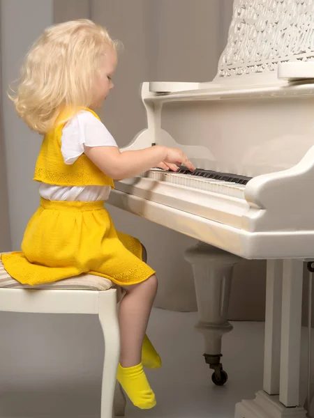 Menina bonita está tocando em um piano de cauda branco. — Fotografia de Stock