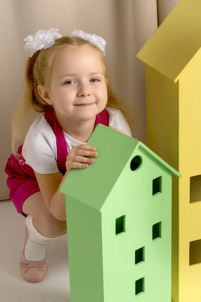 A little girl looks out from behind a toy wooden house. — Stock Photo, Image