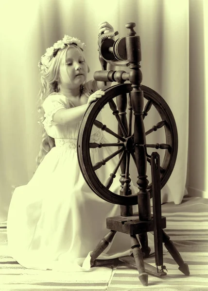 Uma menina bonito teceu uma lã com uma roda rotativa . — Fotografia de Stock