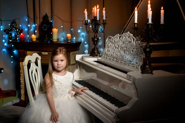 Klein meisje speelt piano bij kaarslicht. — Stockfoto