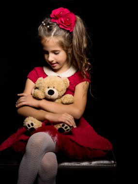 Siyah arka planda oyuncak ayısı olan küçük bir kız..