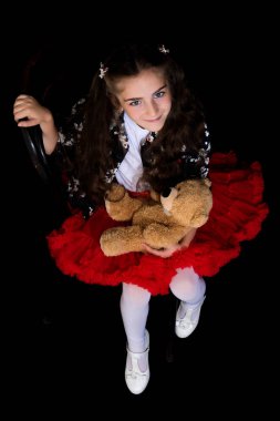 Siyah arka planda oyuncak ayısı olan küçük bir kız..