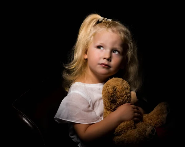 Little girl with a teddy bear on a black background. — Stock Photo, Image