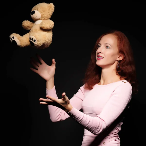 Red-haired girl model posing with a teddy bear. On a black backg