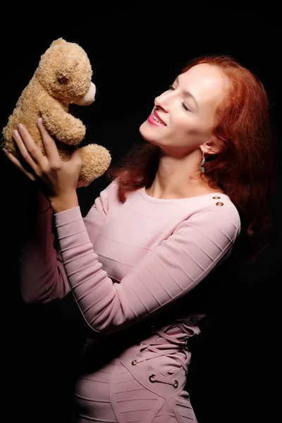 Modelo de chica pelirroja posando con un oso de peluche. En un respaldo negro —  Fotos de Stock