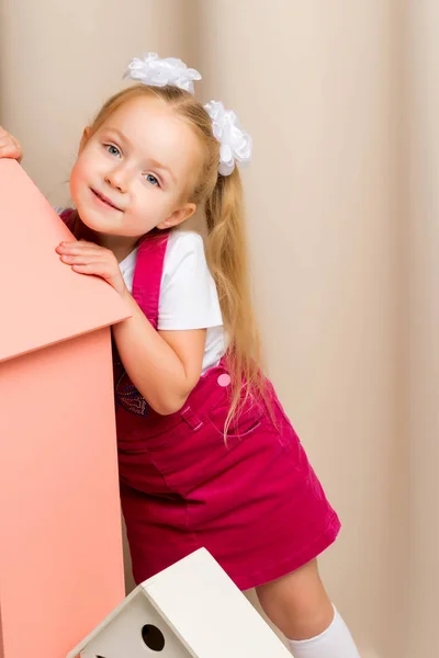Маленькая девочка смотрит из-за игрушечного деревянного дома . — стоковое фото