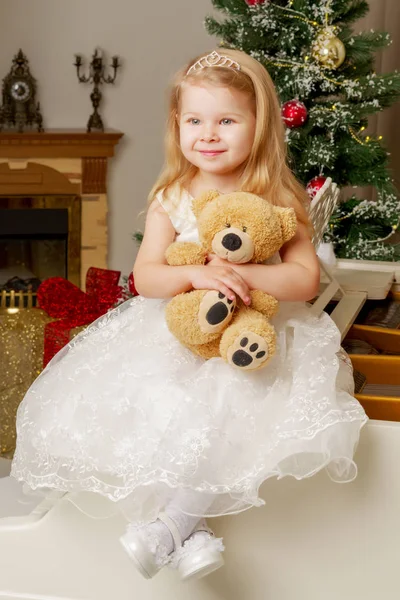 Una bambina è seduta su un pianoforte bianco con un orsacchiotto. — Foto Stock