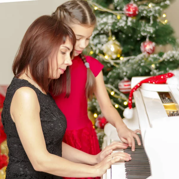 Мама и дочь в новом году возле белого фортепиано . — стоковое фото