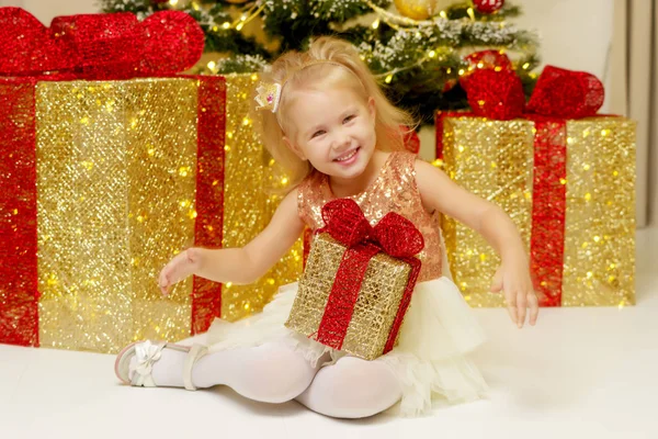 Kleines Mädchen neben dem Weihnachtsbaum mit einem Geschenk. — Stockfoto