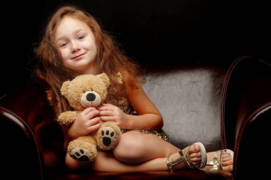 Siyah arka planda oyuncak ayısı olan küçük bir kız..