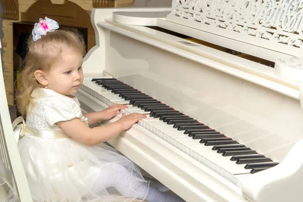 En vacker liten flicka spelar på en vit flygel. — Stockfoto