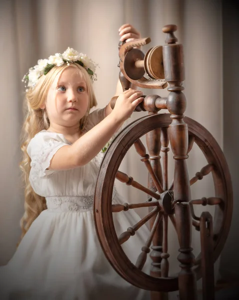 Uma menina bonito teceu uma lã com uma roda rotativa . — Fotografia de Stock