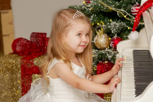 Liten flicka nära piano och julgran. — Stockfoto