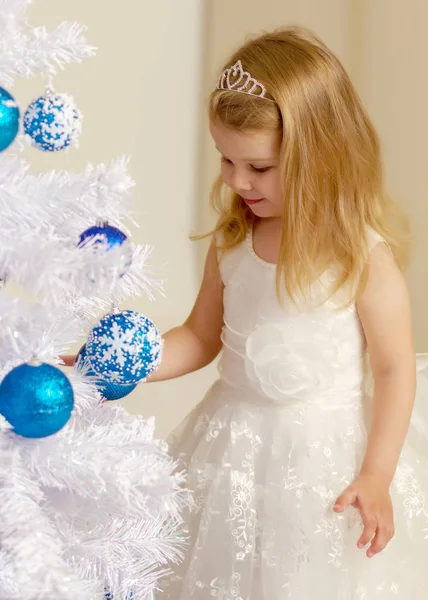 Ein kleines Mädchen schmückt einen Weihnachtsbaum. — Stockfoto