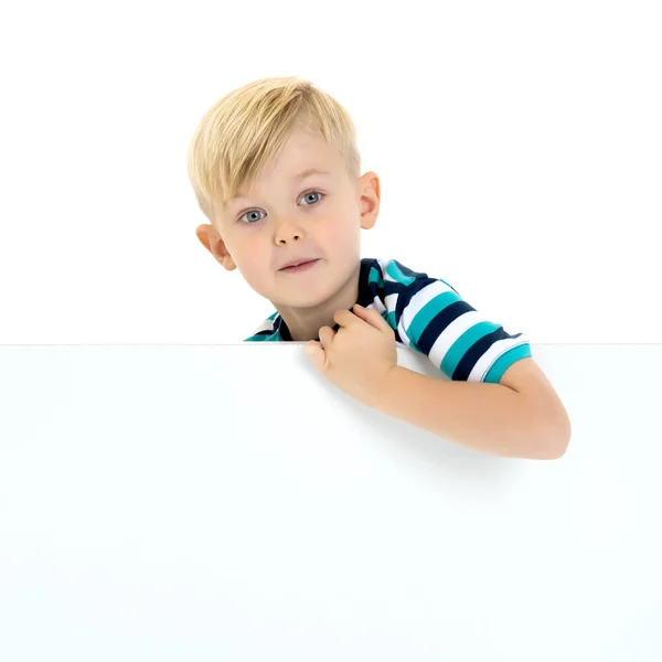 Een kleine jongen is op zoek achter een lege banner. — Stockfoto