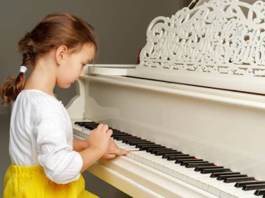 Güzel küçük kız beyaz bir piyanoda çalıyor..
