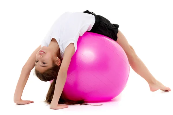 Klein meisje doet oefeningen op een grote bal voor fitness. — Stockfoto