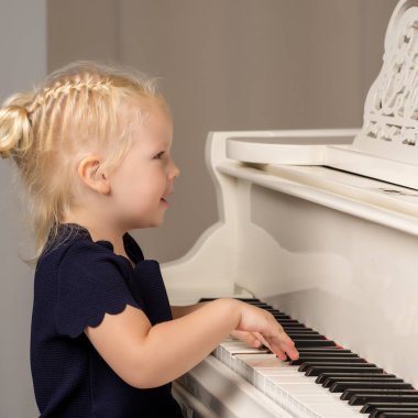 Güzel küçük kız beyaz bir piyanoda çalıyor..
