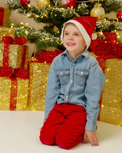 Bir hediye ile Noel ağacı yanında küçük bir çocuk. — Stok fotoğraf