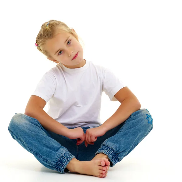 Une petite fille est assise sur le sol dans un T-shirt blanc propre. — Photo