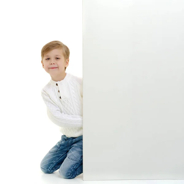 Un niño pequeño está mirando detrás de una pancarta vacía . —  Fotos de Stock