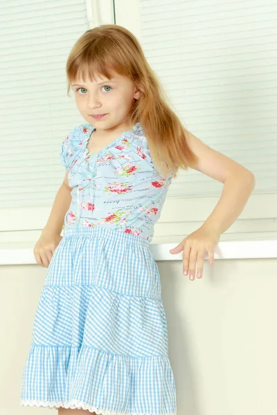 A little girl is sitting by the window with jalousie — Stock Photo, Image