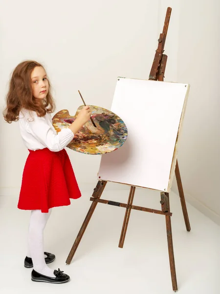 Petite fille avec une palette et une brosse près du chevalet . — Photo