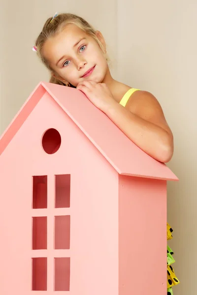 Una bambina guarda fuori da dietro una casa di legno giocattolo . — Foto Stock