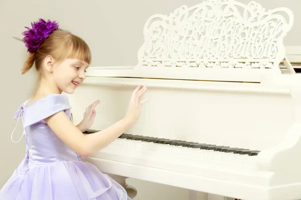 Uma menina está posando perto de um piano de cauda branco . — Fotografia de Stock