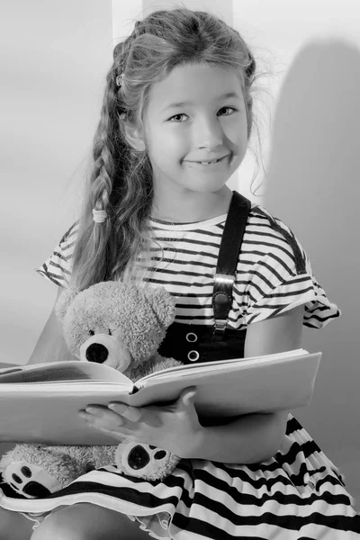 Menina está lendo um livro para um ursinho de pelúcia . — Fotografia de Stock