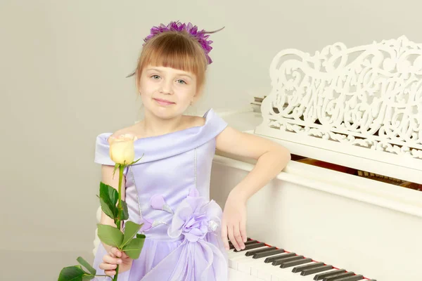 Uma menina está posando perto de um piano de cauda branco . — Fotografia de Stock