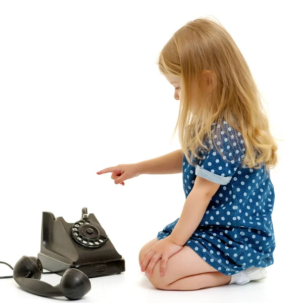 En lille pige ringer på den gamle telefon. - Stock-foto