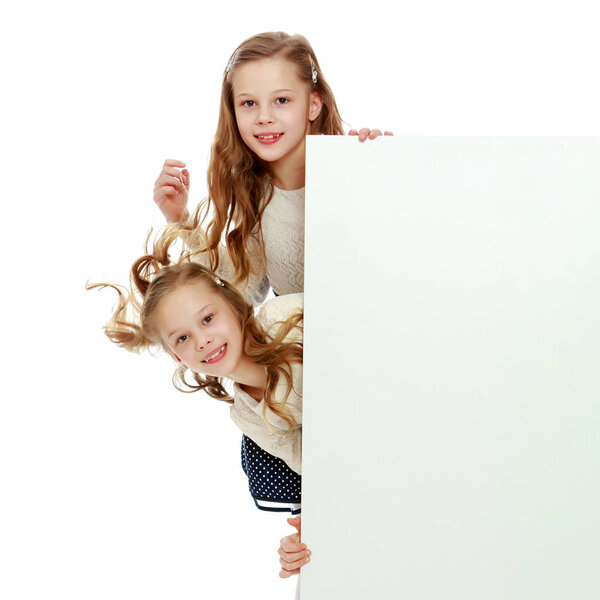 Two little girls peeking out from behind a white advertising ban