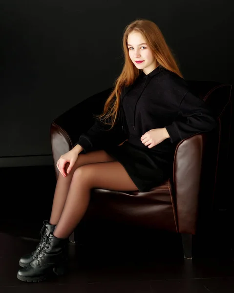 Uma adolescente está sentada em uma cadeira de couro . — Fotografia de Stock