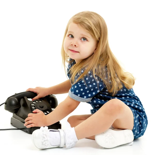 En liten flicka ringer i den gamla telefonen.. — Stockfoto