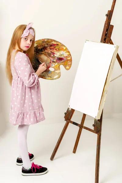 Petite fille avec une palette et une brosse près du chevalet . — Photo