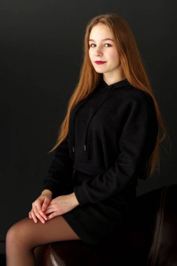 Bir genç kız bir deri sandalyede oturuyor.