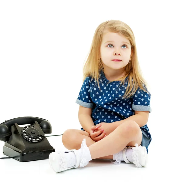 En liten flicka ringer i den gamla telefonen.. — Stockfoto