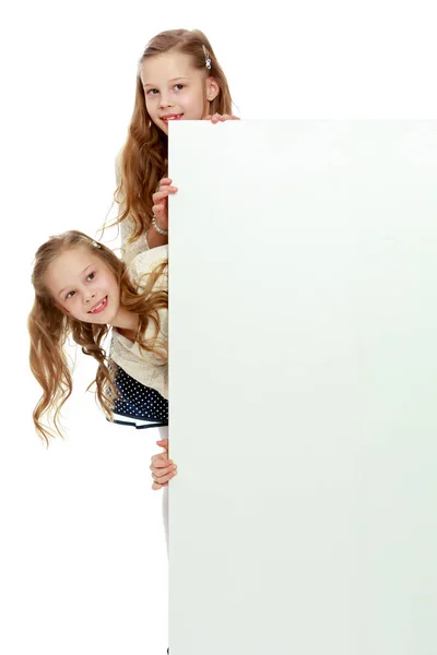 Due ragazzine sbirciano da dietro un divieto pubblicitario bianco — Foto Stock