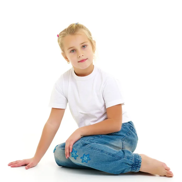 En liten flicka sitter på golvet i en ren vit t-shirt. — Stockfoto