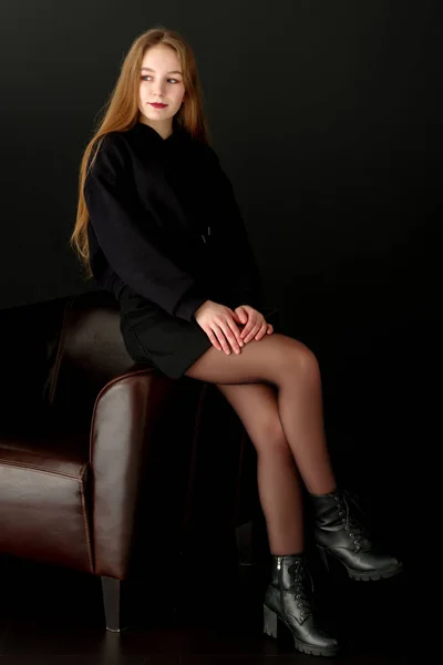 En tonårig flicka sitter på en skinnfåtölj. — Stockfoto