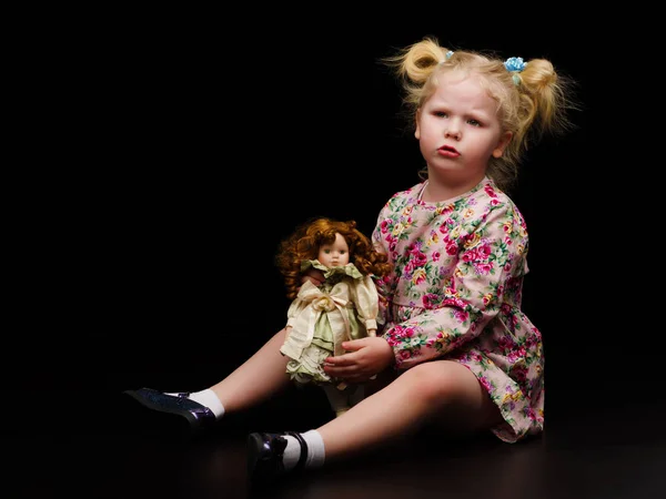 少女は黒を背景に人形と遊ぶ. — ストック写真