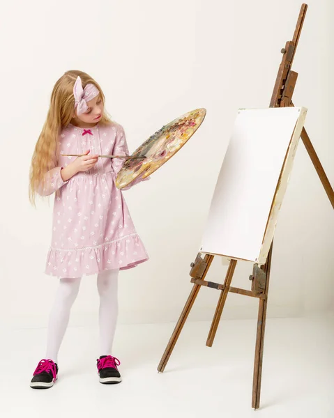 Malá holčička s paletou a štětcem poblíž stojan. — Stock fotografie