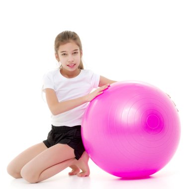 Küçük kız spor yapmak için büyük bir top üzerinde egzersiz yapıyor..