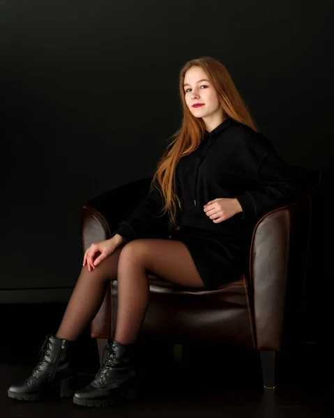 En tonårig flicka sitter på en skinnfåtölj. — Stockfoto