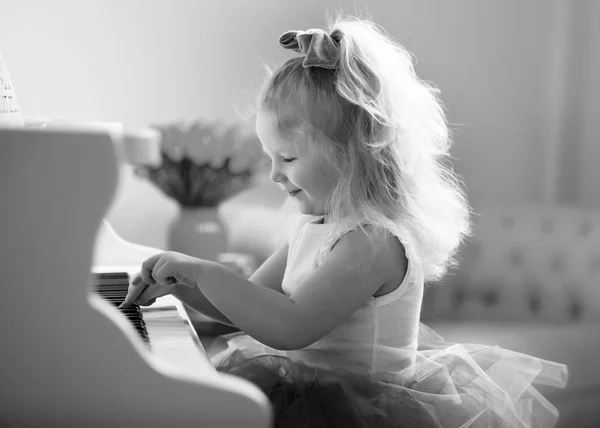 Menina bonita está tocando em um piano de cauda branco. — Fotografia de Stock